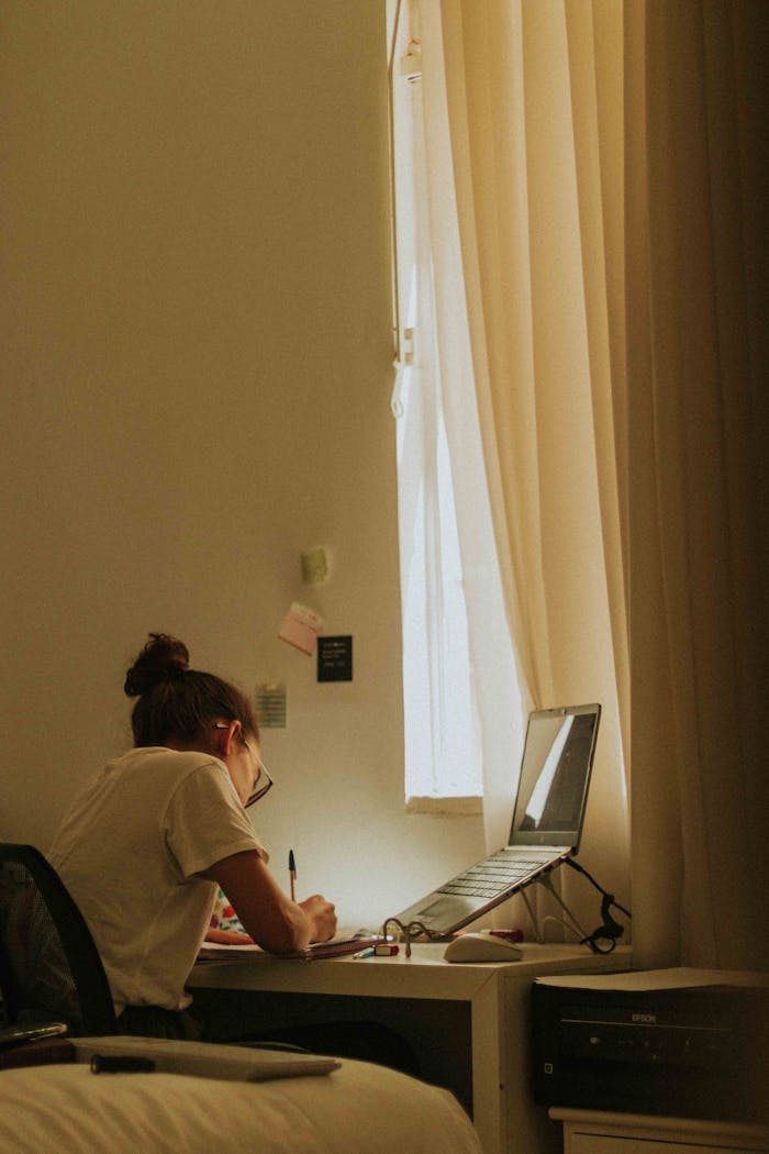 A young woman writing at a desk by a window, bathed in soft light, illustrating concentration.