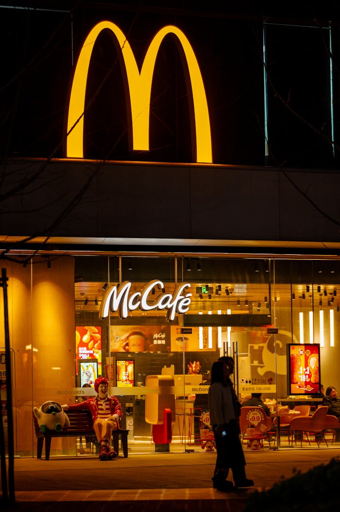 creative-03 A person walks past a McDonald's McCafé at night, illuminated by the iconic golden arches.